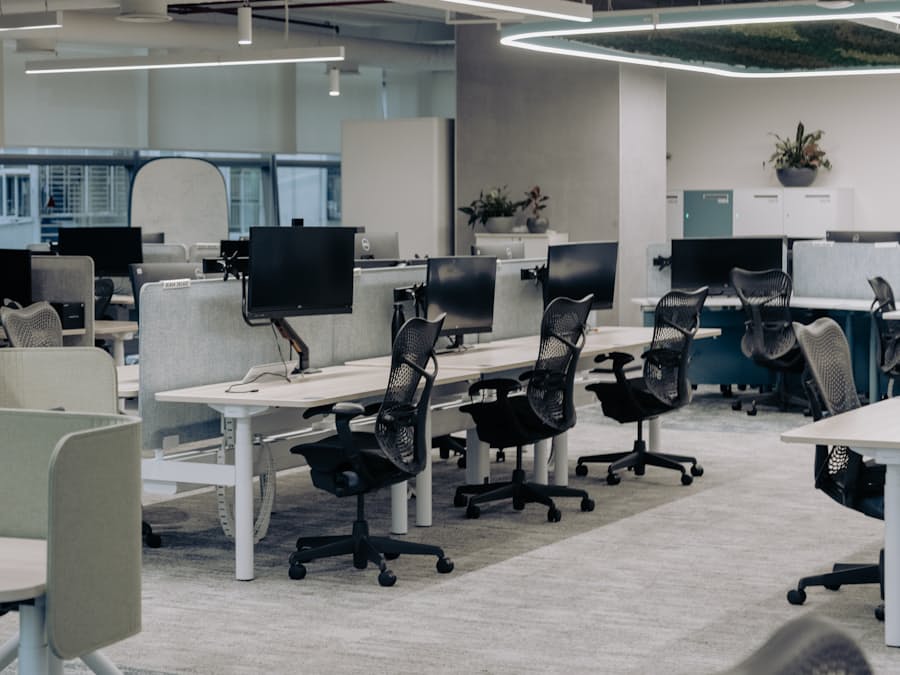 An empty open-plan office with sit-stand desks, monitors and mesh chairs