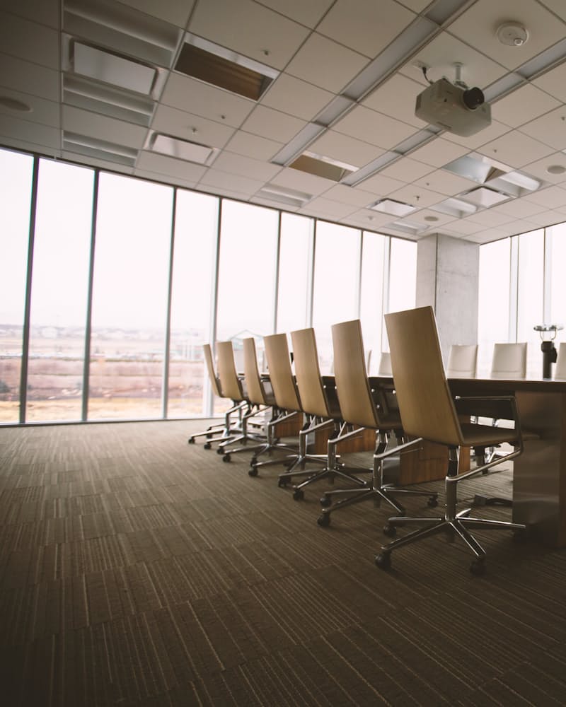 An empty boardroom with a long table, a row of high-backed chairs and a wall of windows