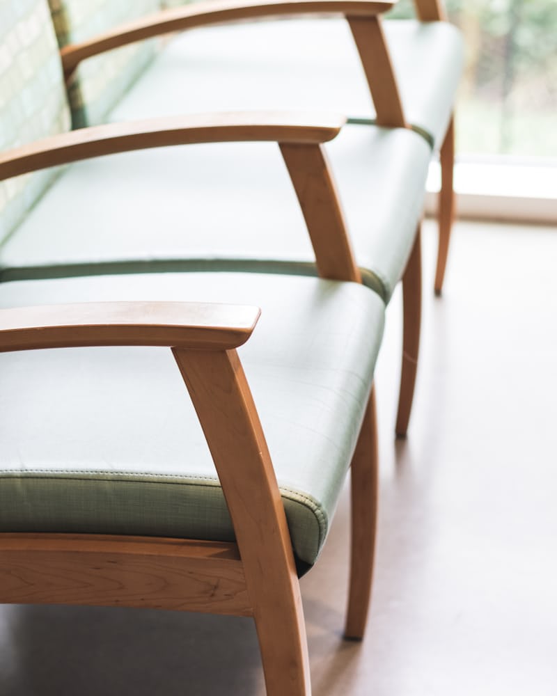 A row of wooden waiting-room chairs with pale green seats beside a window