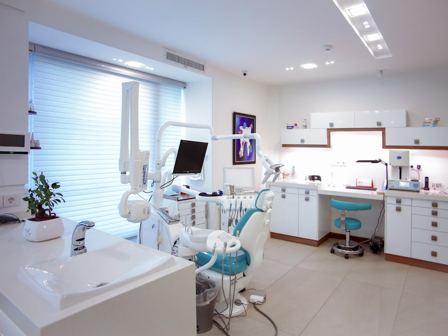 A bright, empty dental surgery with a teal treatment chair, an overhead light and a monitor arm