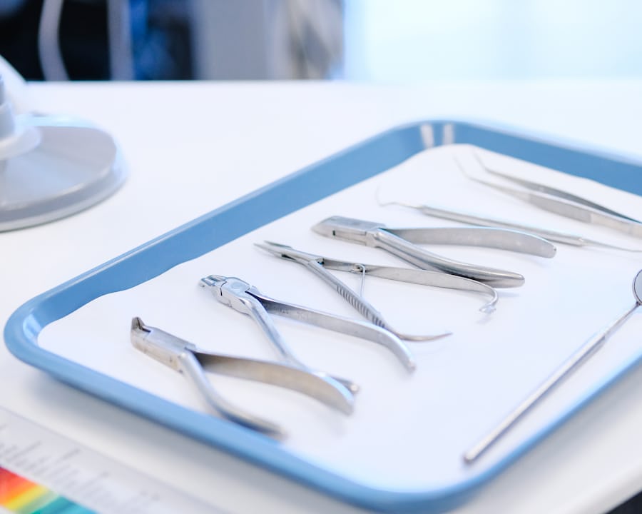 A blue instrument tray on a white worktop holding dental forceps, a probe and tweezers