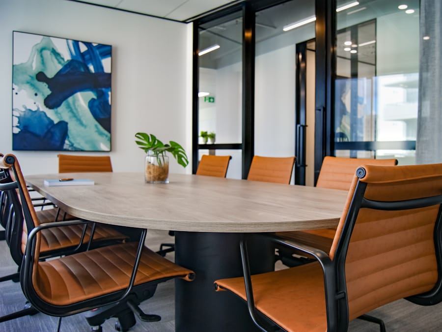 An empty meeting room with an oval table, tan leather chairs, a potted plant and a glazed wall