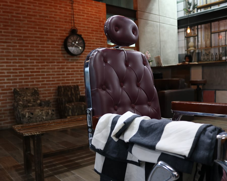 A burgundy leather barber chair with a striped towel over one arm, against an exposed brick wall