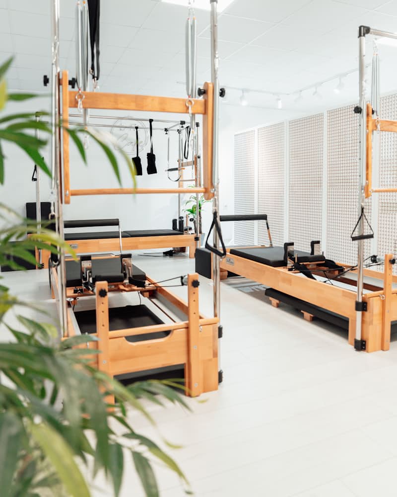A bright empty pilates studio with three wooden reformers, rattan screens and a plant