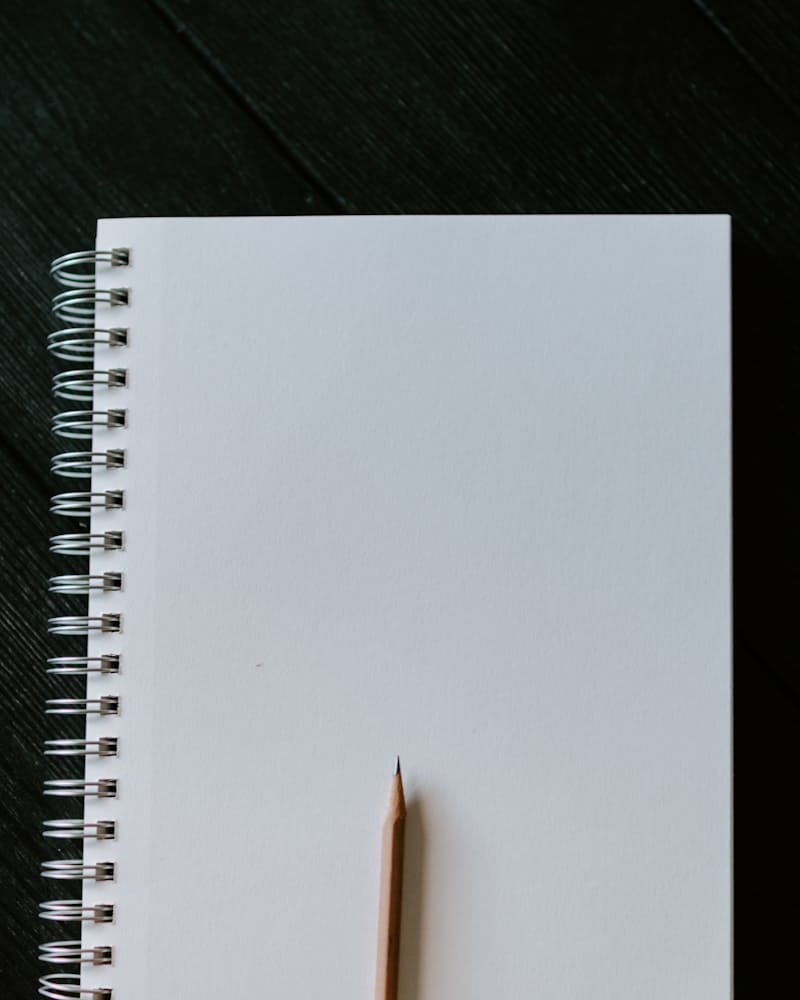 A blank spiral notebook and a sharpened pencil on a dark wooden desk