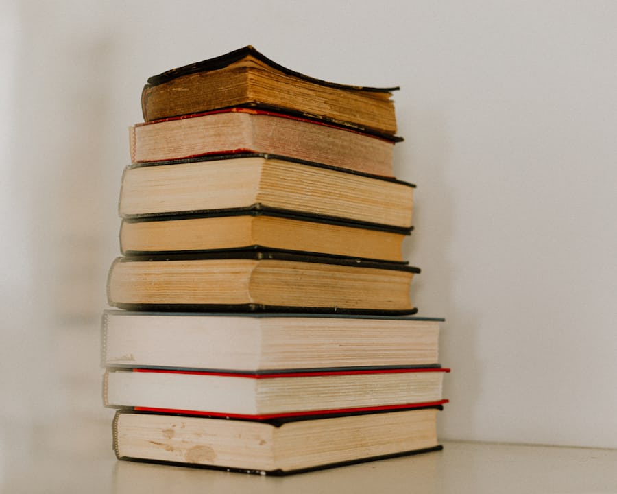 A stack of eight hardback books on a pale surface